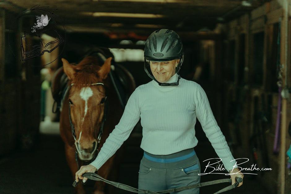 Woman Wearing an Equestrian Helmet Guiding a Horse Out of the Stable