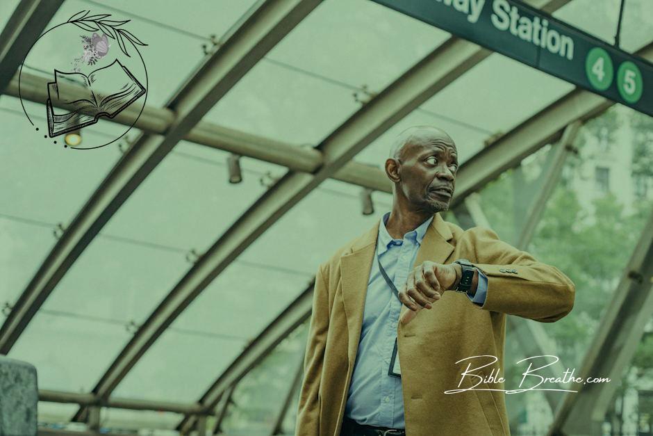 Serious African American businessman in formal clothes standing in subway station and checking time on wristwatch while looking away thoughtfully