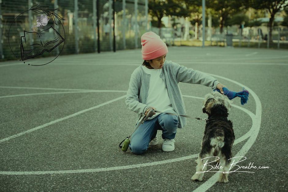 Ethnic kid showing command to intelligent dog while squatting on asphalt pavement in city