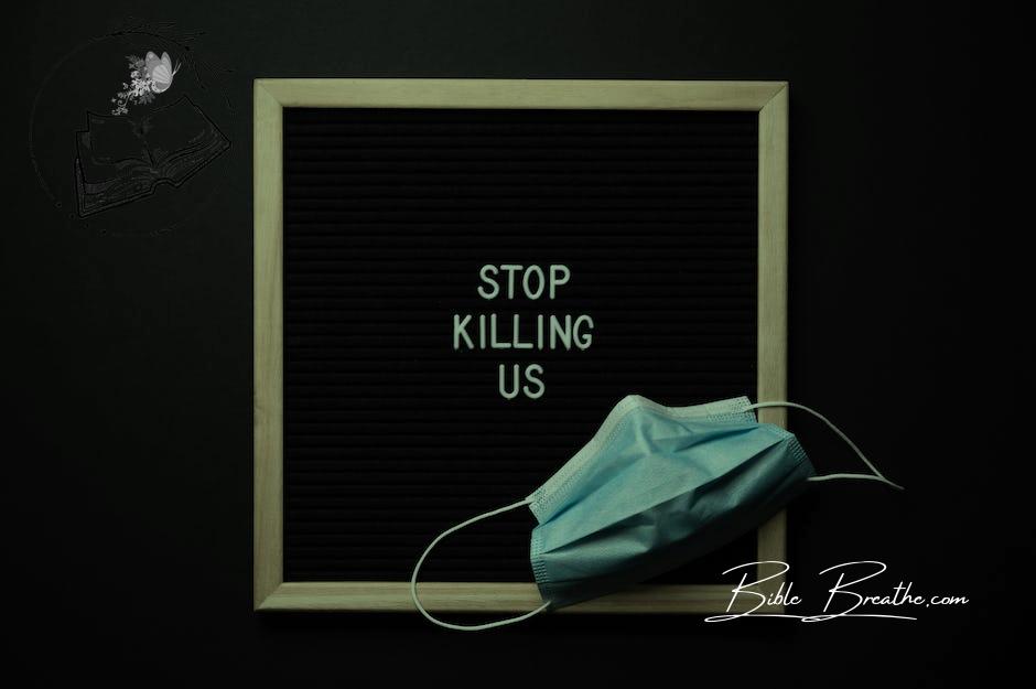 Top view of composition of blackboard with written phrase STOP KILLING US under mask against black background