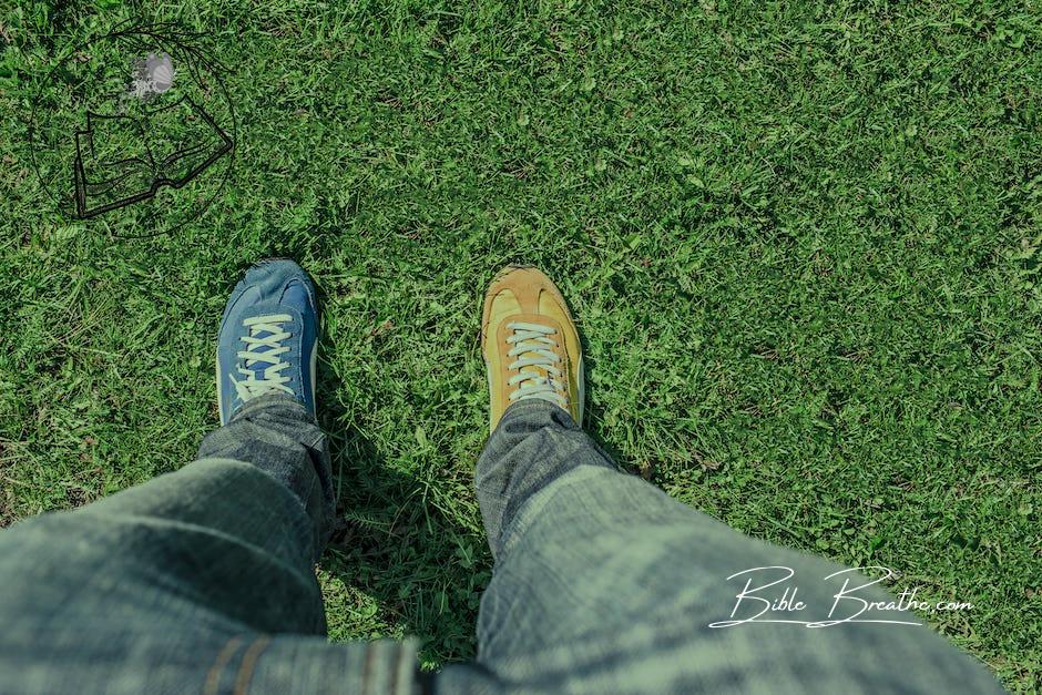 Person Wearing Unpaired Running Shoes Standing on Green Grass