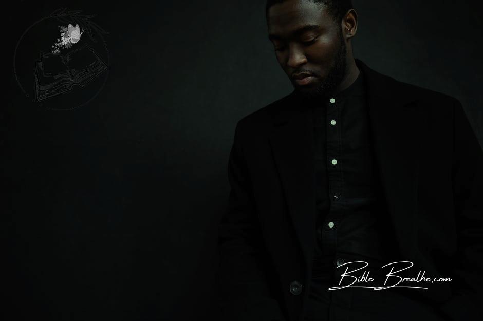 Serious black man in black suit standing in studio