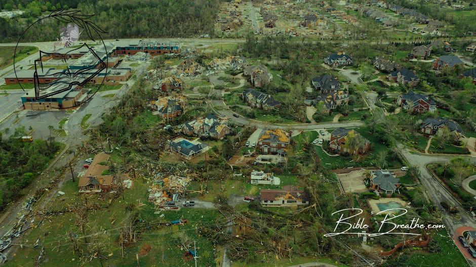 Aerial view of tornado impact on small settlement cottages with destroyed roofs windthrown trees and bent electricity transmission lines