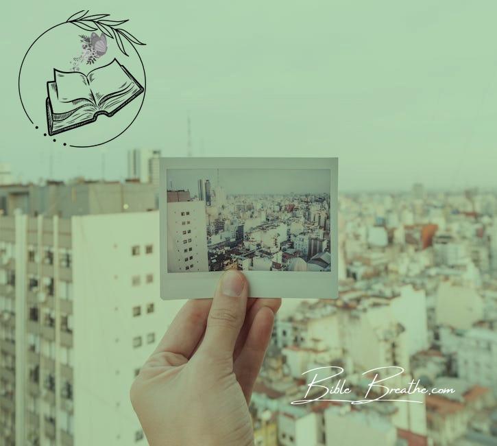 Hand of a Person Holding a Photograph of a City Against the Real Buildings