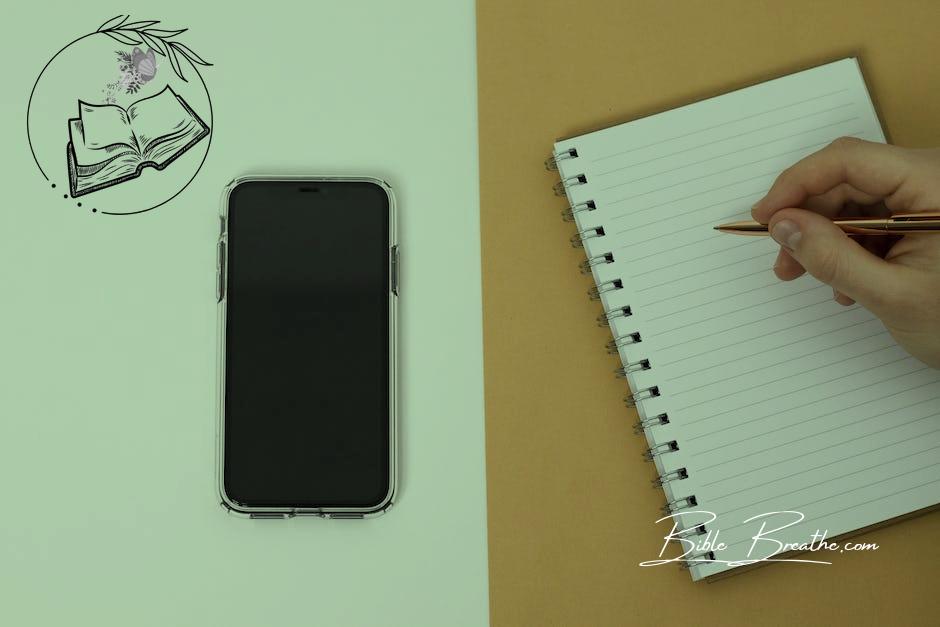 A Cell Phone and a Person Writing in a Notebook