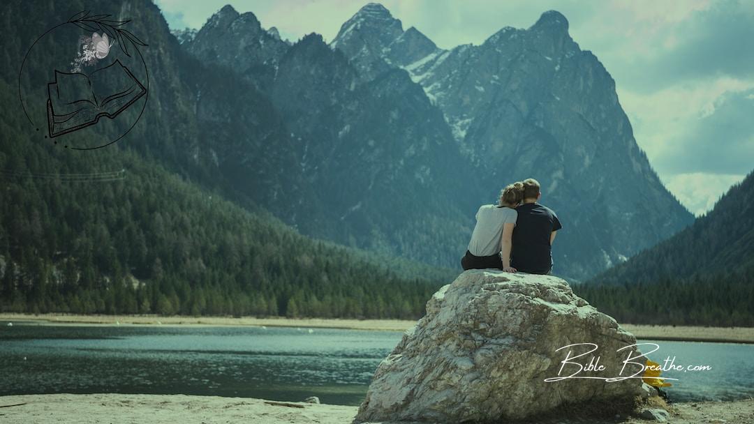 a couple sits on a rock looking out over a lake