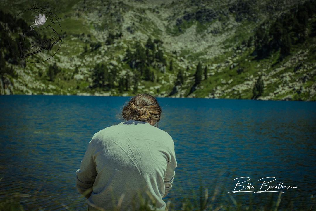 man in white long sleeve shirt sitting on green grass near body of water during daytime
