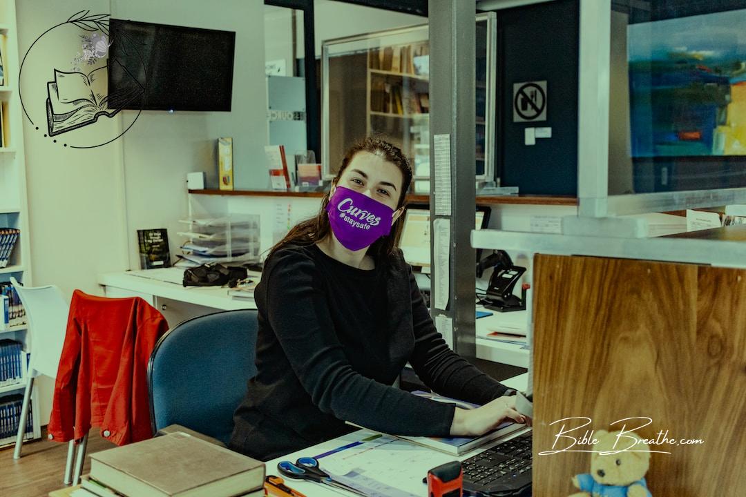 a woman sitting at a desk with a purple mask on her face