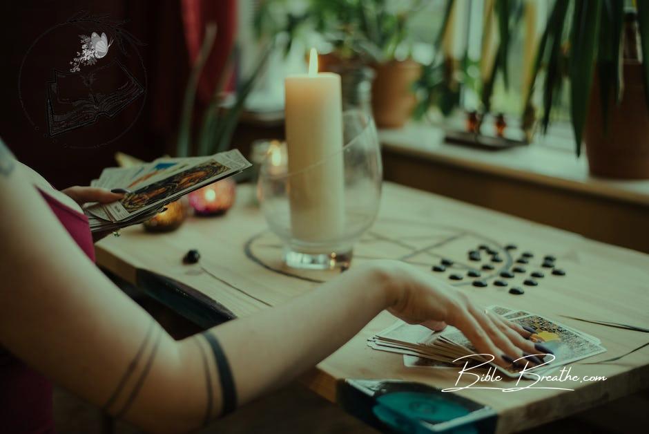 Crop unrecognizable fortune teller predicting fate with tarot cards near shiny candle at home
