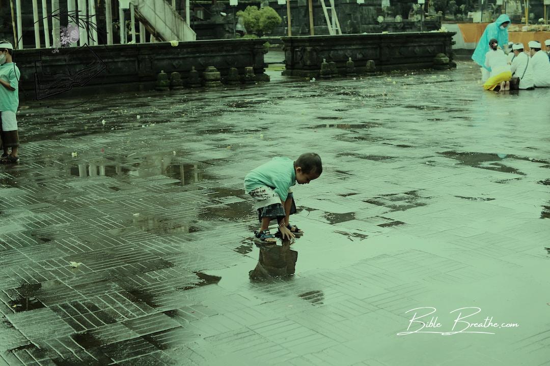 a little boy playing in the rain with a puddle