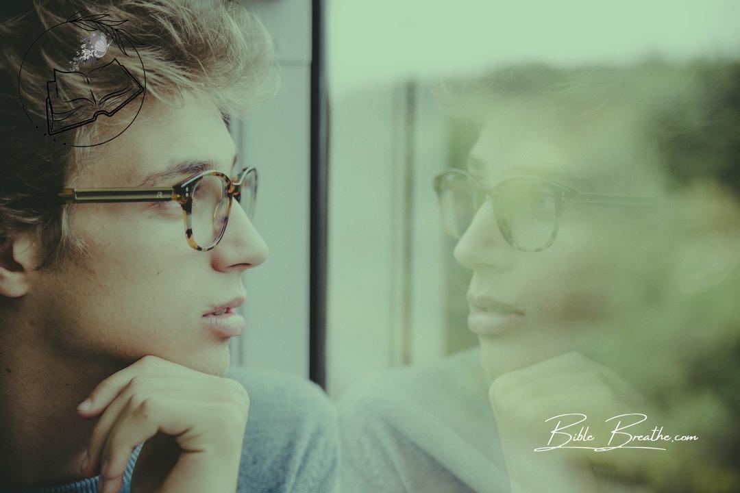 a man wearing glasses looking out a window