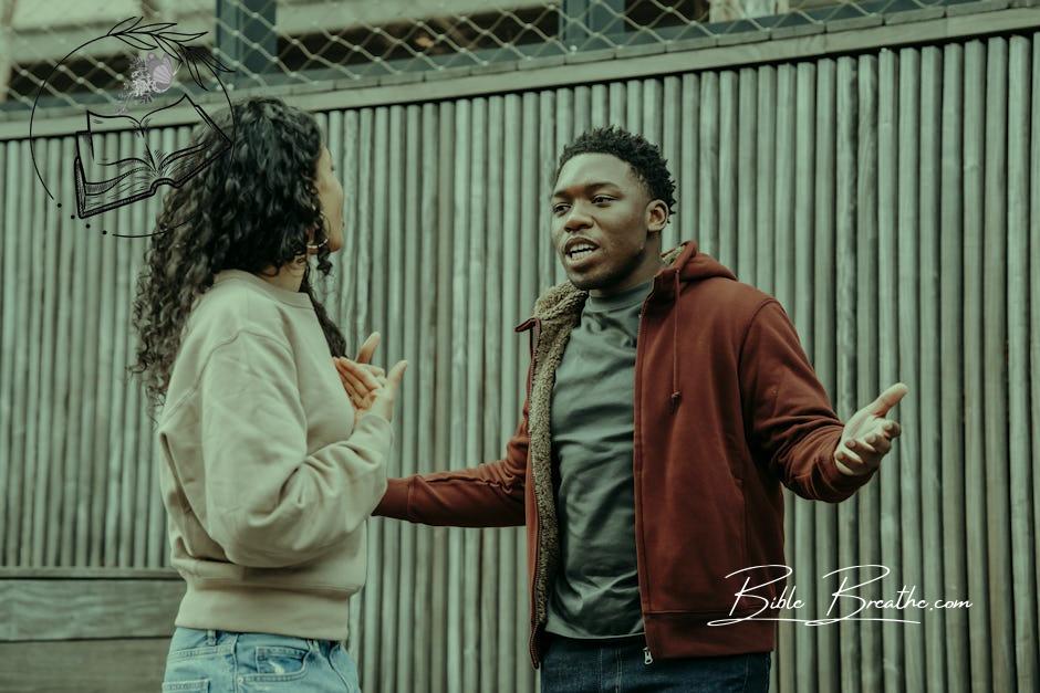 Angry African American boyfriend and ethnic girlfriend looking at each other while having emotional dispute on street near wooden fence